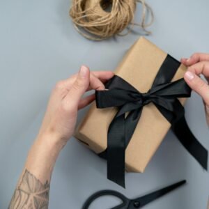 Close-up of hands wrapping a gift box with a black ribbon, ready for gifting.